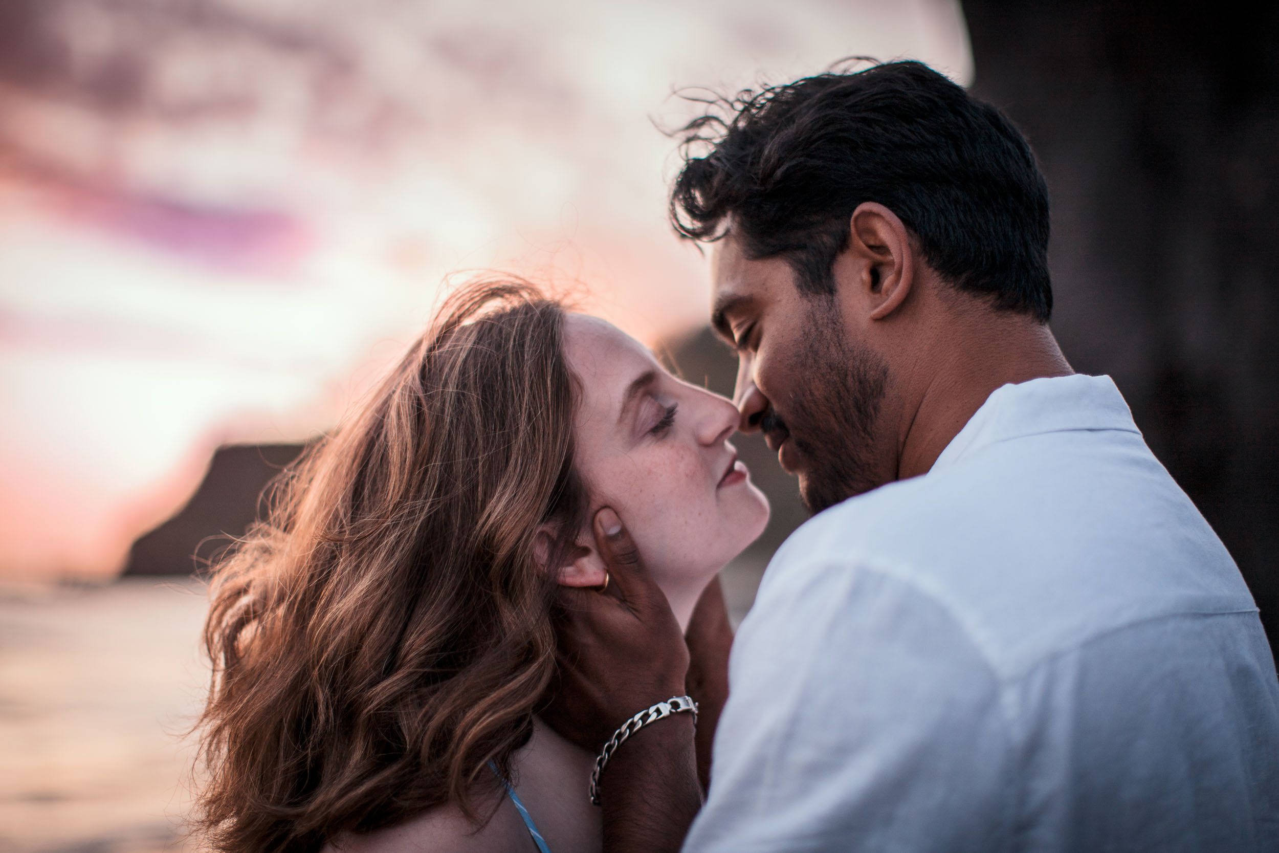 Couple about to kiss under a pink sunset sky at Praia Formosa, Madeira